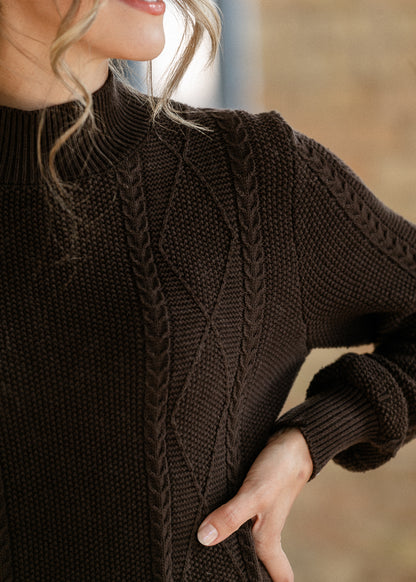 Close-up of chocolate brown sweater dress showing cable knit texture, diamond stitching, and ribbed mock neckline.

