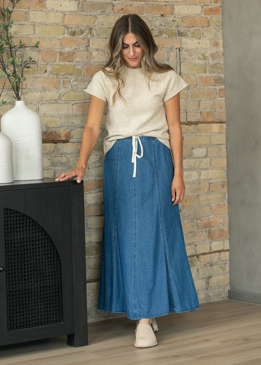Blue denim maxi skirt with drawstring waistband, paneled construction, and full flowing hem.