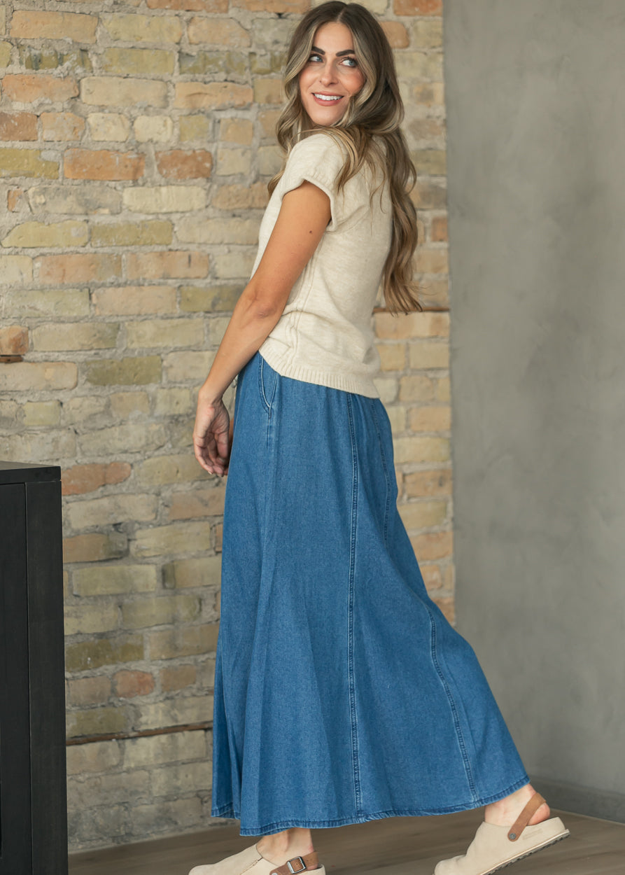 Back view of medium wash denim maxi skirt showing vertical panel seams and flared shape.