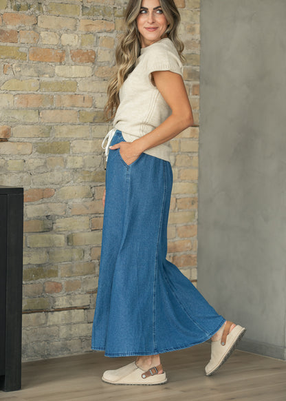 Long blue denim maxi skirt with flowing paneled silhouette and ankle-length hem.