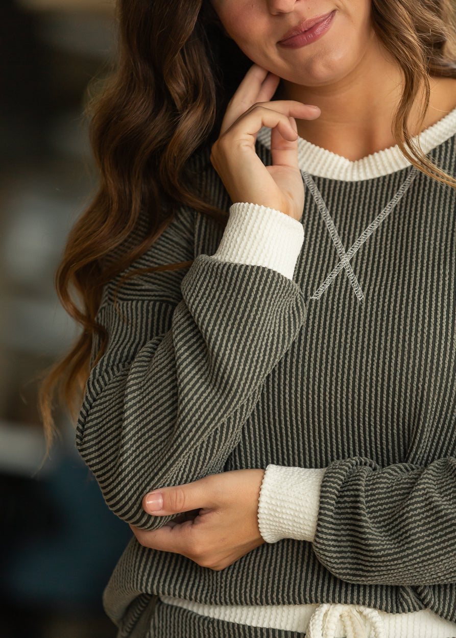 Close-up of olive ribbed round neck pullover with cream contrast trim and decorative chest stitching.