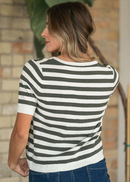 Olive and ivory striped knit top with ribbed hem, back view against a brick wall backdrop.