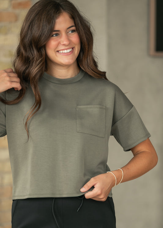 Olive crew neck scuba top with short sleeves and functional chest pocket, styled with a black athletic maxi skirt.