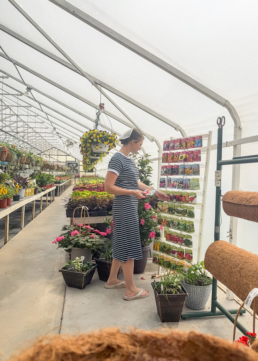 Woman shopping for plants in a greenhouse in navy and white striped midi T-shirt dress with short raglan sleeves