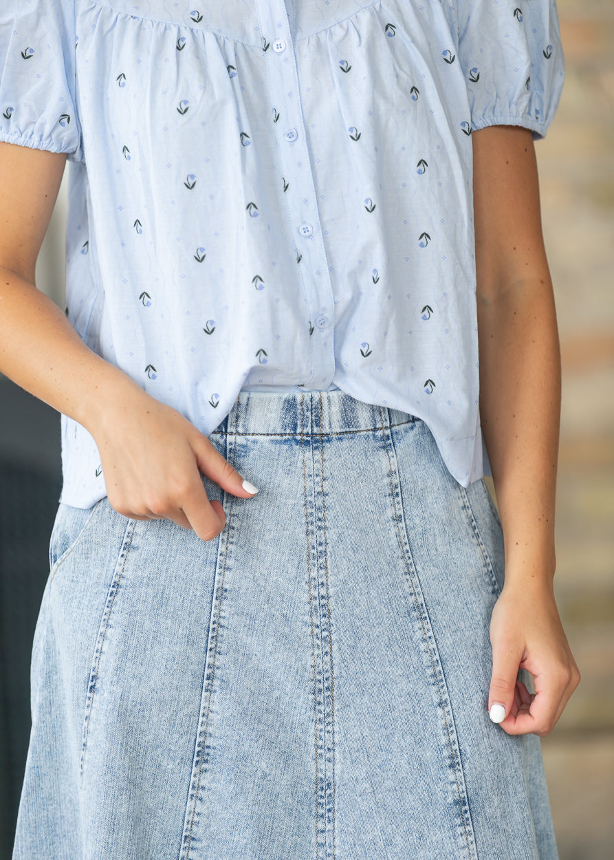 Close-up of the light wash denim skirt showing paneled seams and elastic waistband.
