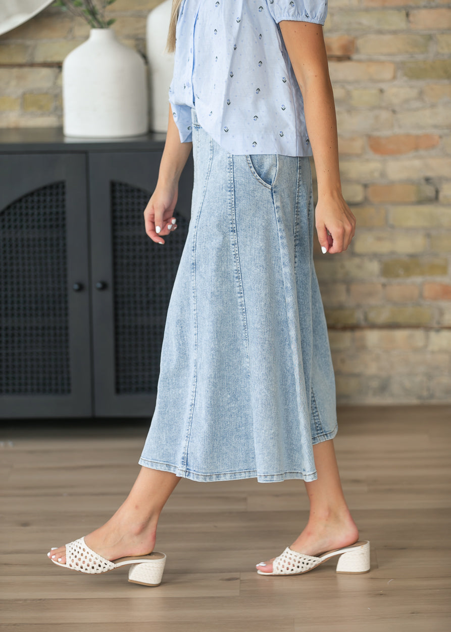 Side view of a light wash denim midi skirt with side pockets and A-line shape.
