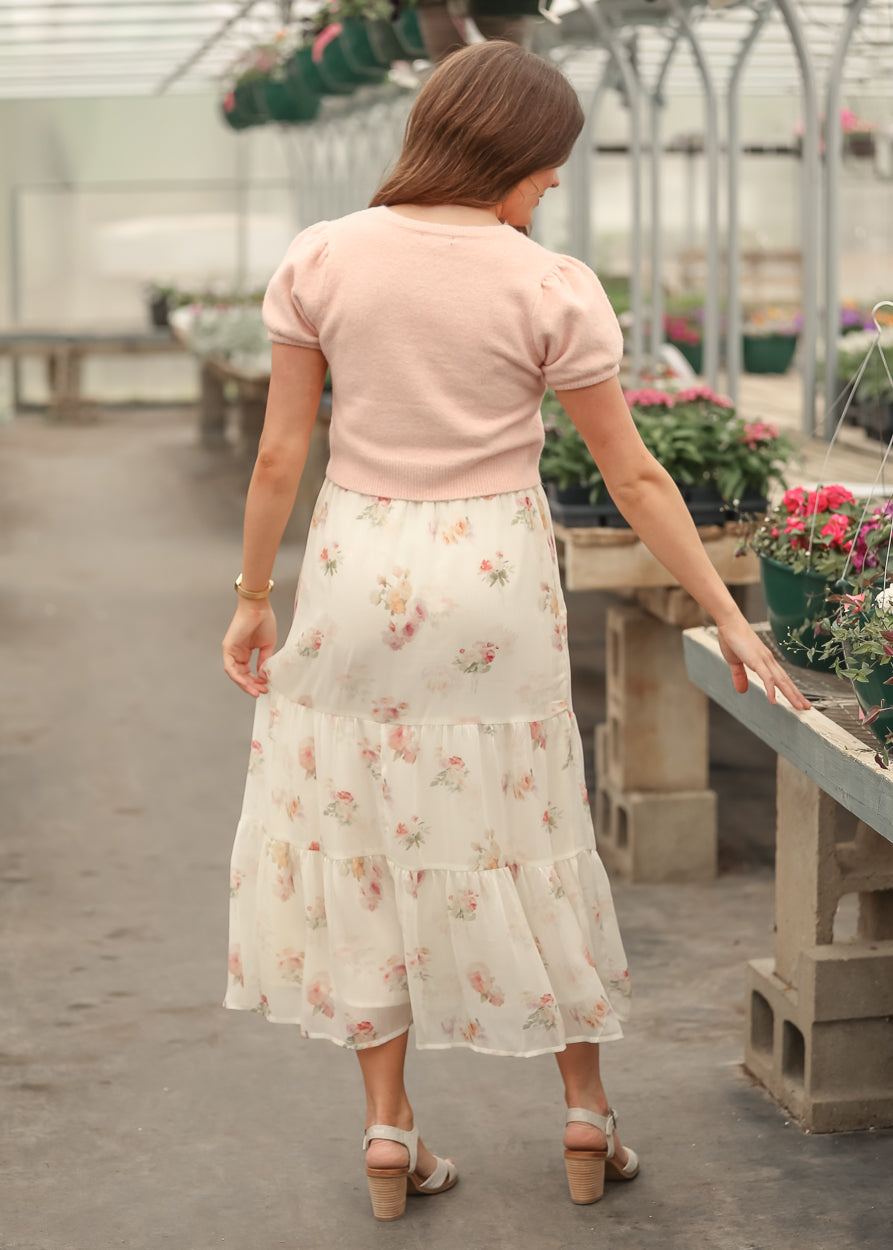 Soft pink cropped button front cardigan with puff sleeves, back view, styled with a floral cream maxi skirt.