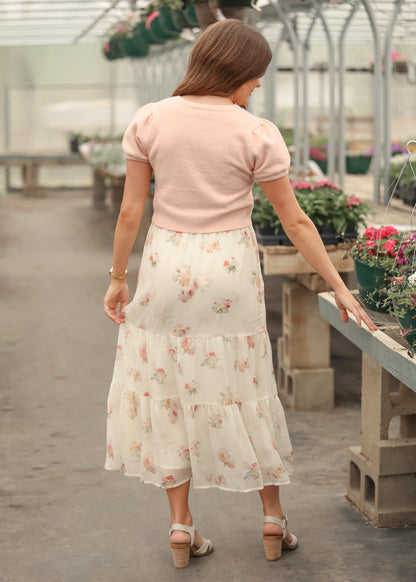 Soft pink cropped button front cardigan with puff sleeves, back view, styled with a floral cream maxi skirt.
