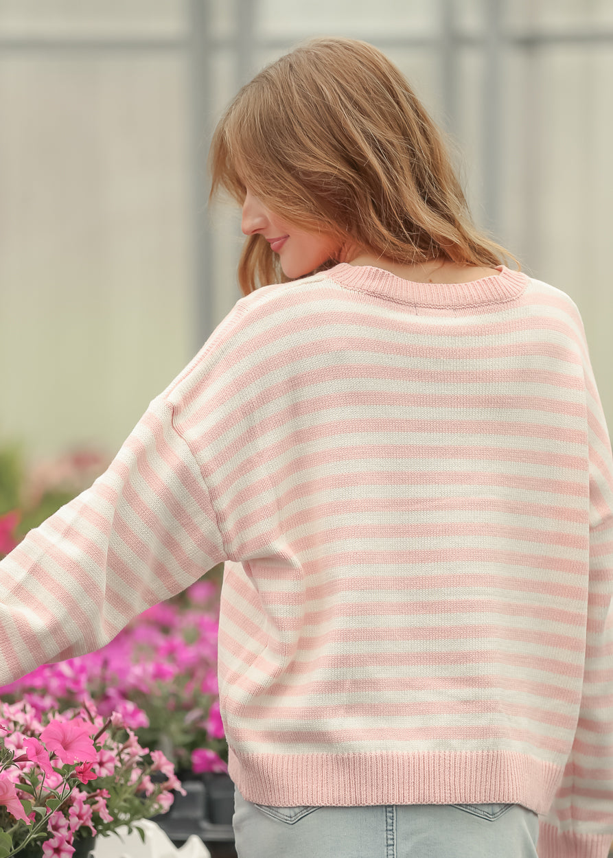 Side view of pink and cream striped knit sweater showing the loose fit and long ribbed sleeves.