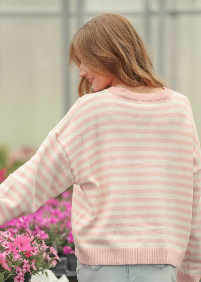 Side view of pink and cream striped knit sweater showing the loose fit and long ribbed sleeves.