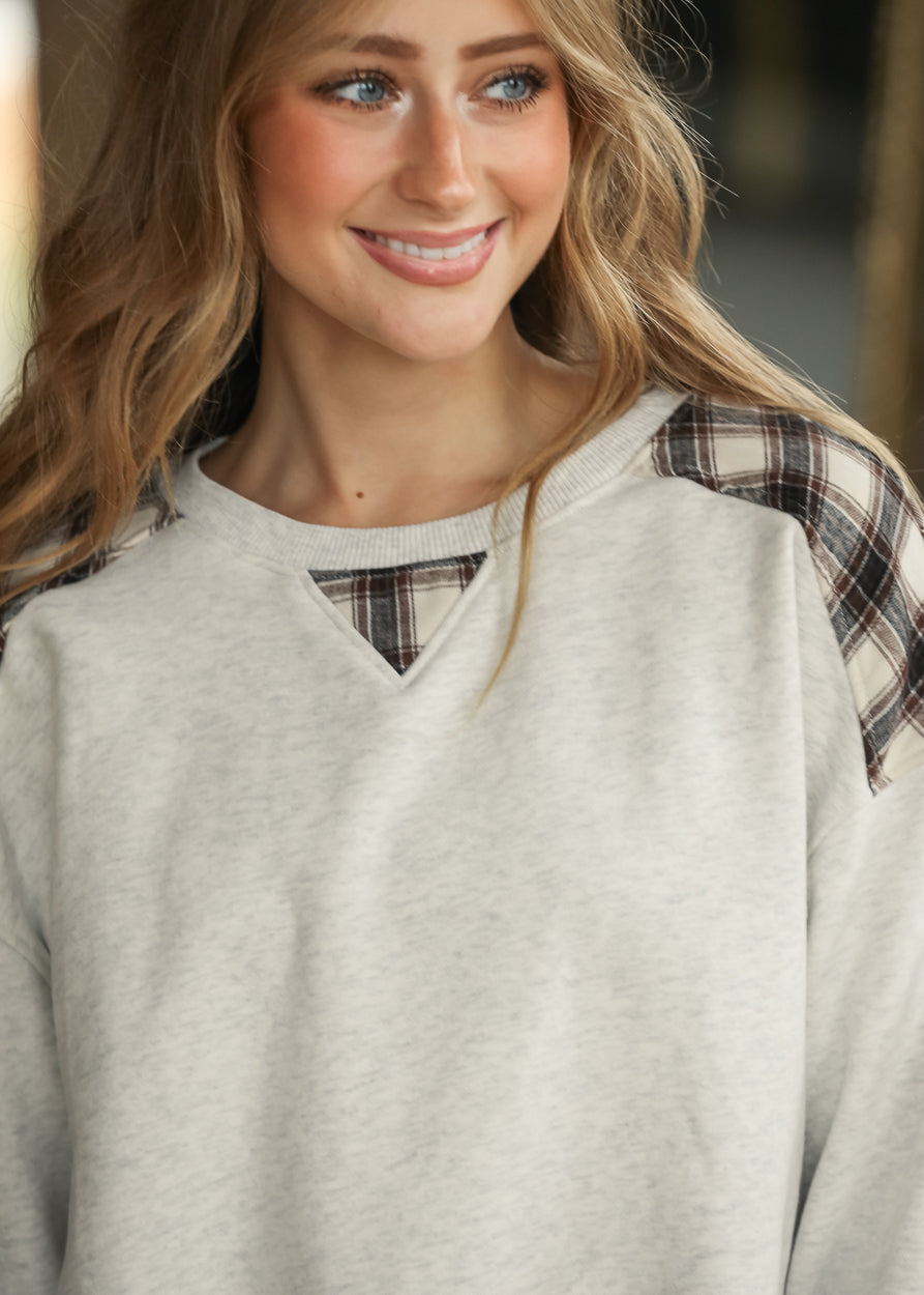Close-up of white mélange sweatshirt showing plaid shoulder panels and triangular plaid neckline inset.