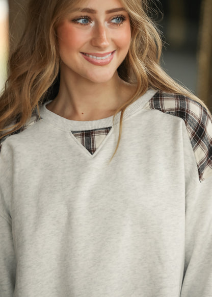 Close-up of white mélange sweatshirt showing plaid shoulder panels and triangular plaid neckline inset.