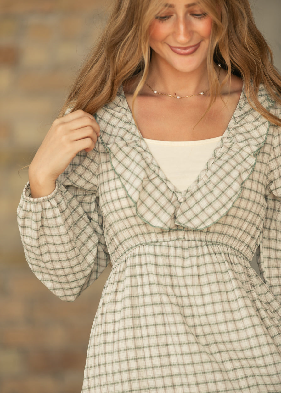 Close-up of cream and sage plaid dress showing the ruffled V-neckline, gathered waist, and elastic cuff.