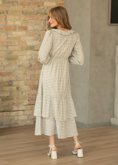 Back of cream plaid midi dress showing the gathered waist, long sleeves, and tiered mid-shin skirt.