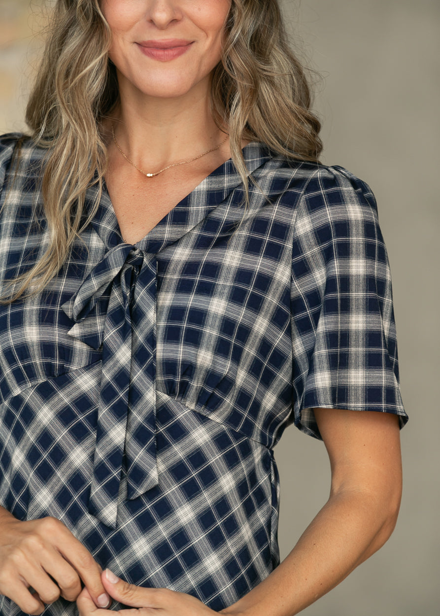 Close-up of navy plaid V-neck dress showing the tie neckline and softly gathered shoulder.