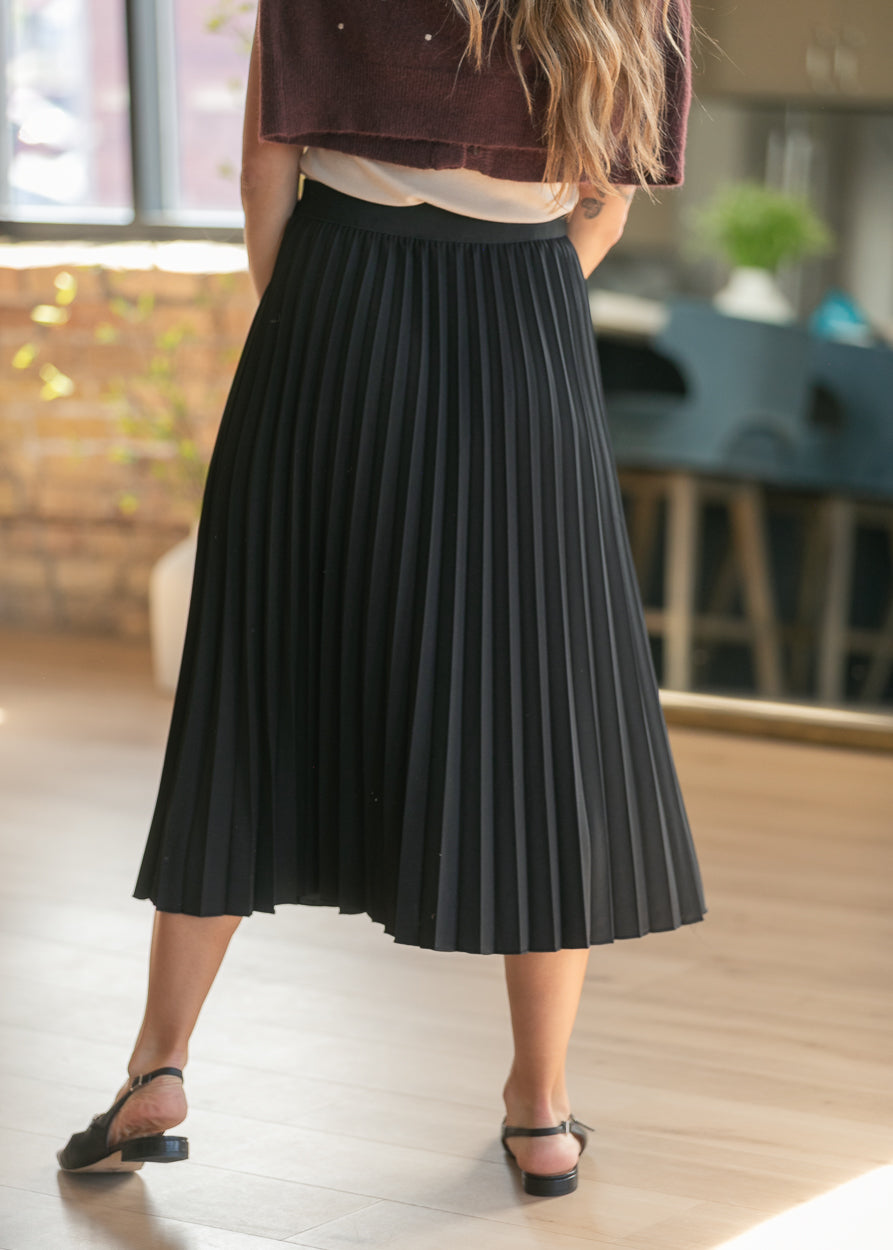 Black pleated midi skirt showing movement and flow as the model walks forward.