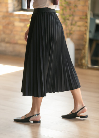 Black pleated midi skirt styled with cream top, maroon vest, and black platform shoes.