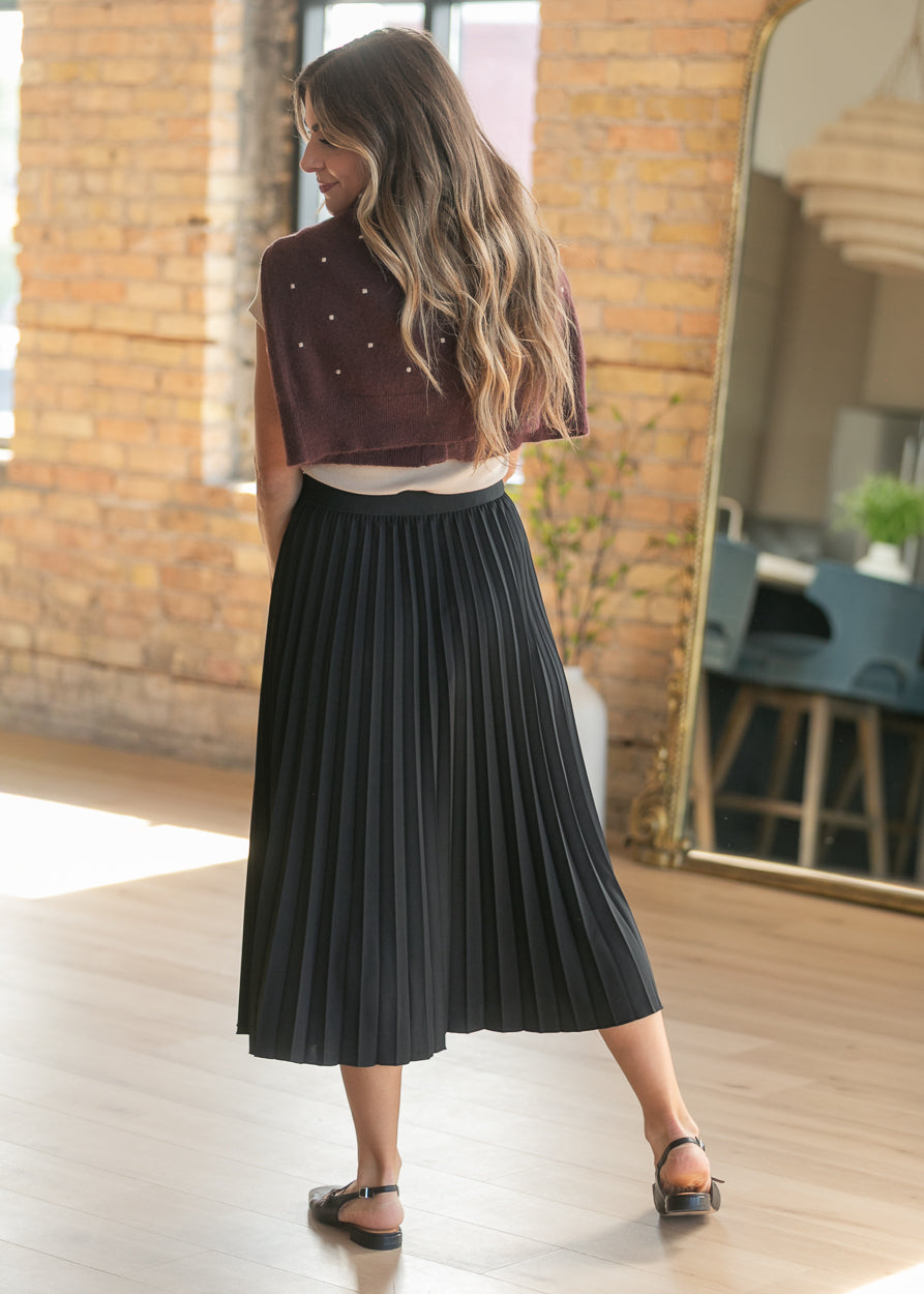 Back view of black pleated midi skirt on model, showing mid-calf length.