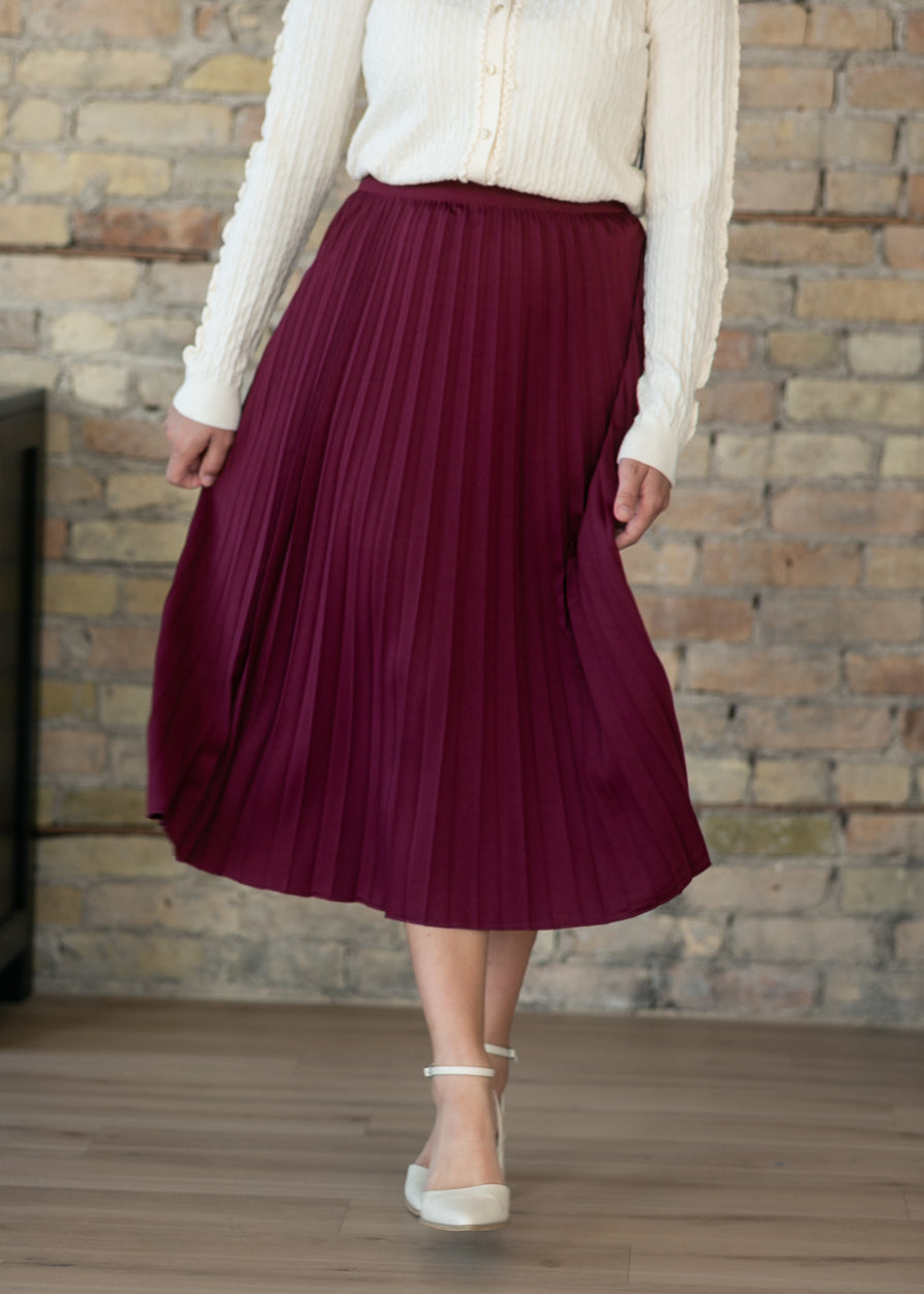 Burgundy pleated midi skirt with stretchy waistband, partial front view showing fabric detail.
