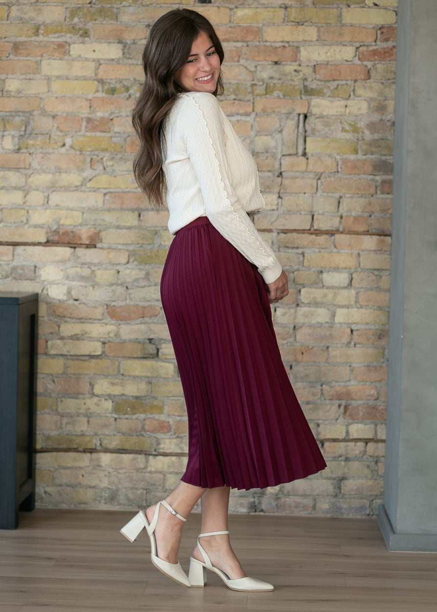 Burgundy pleated midi skirt in loose fit, full-length view on model from behind.
