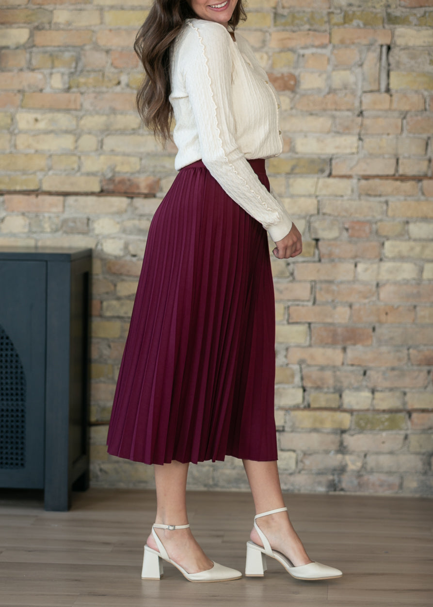 Burgundy pleated midi skirt styled with cream ribbed top and white platform shoes.