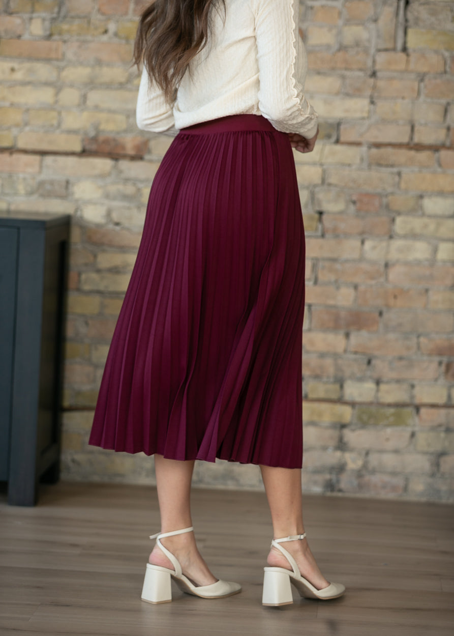 Back view of burgundy pleated midi skirt on model, showing mid-calf length.