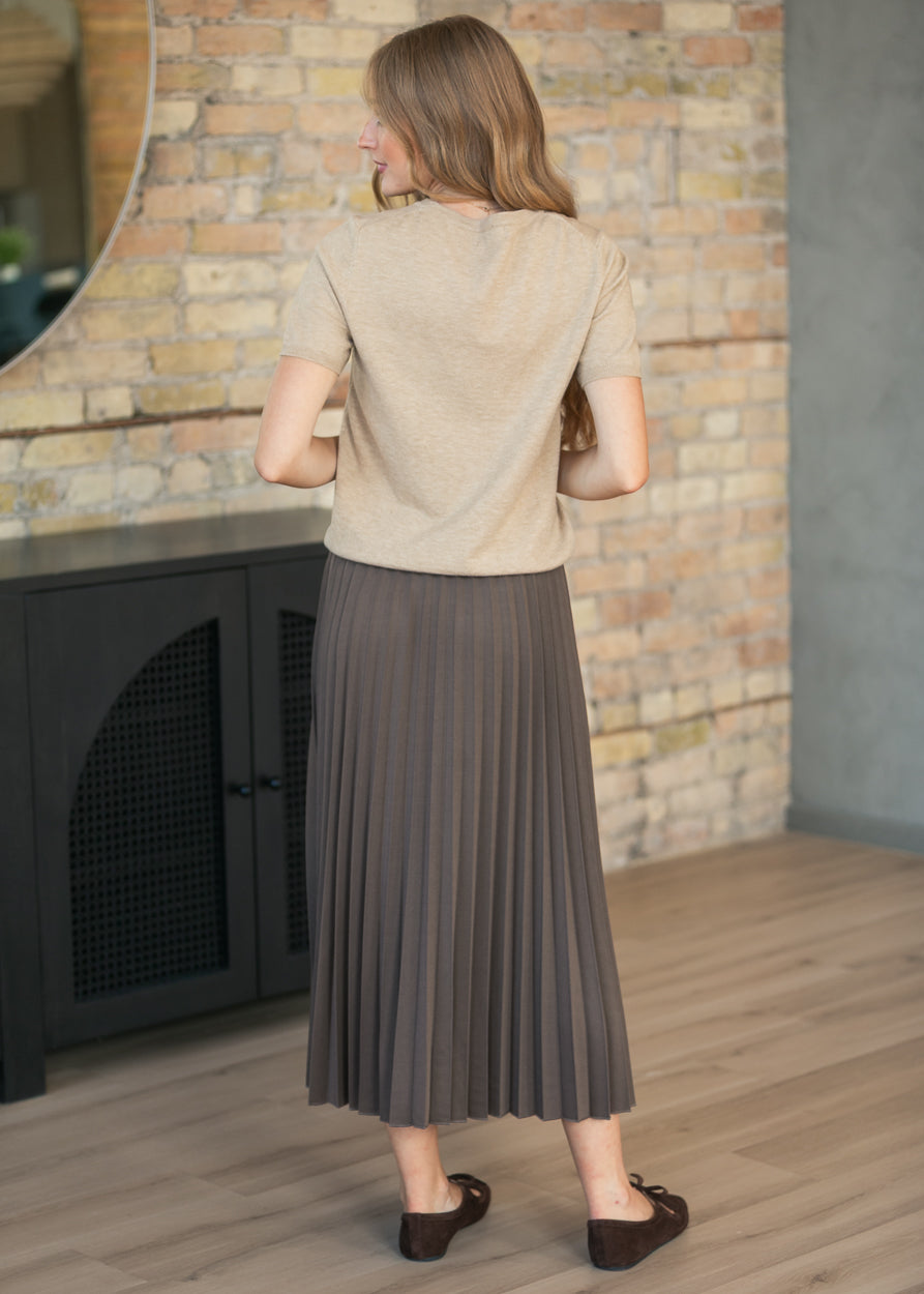 Back of taupe short sleeve sweater showing the relaxed hip-length fit, styled with a cocoa pleated skirt.
