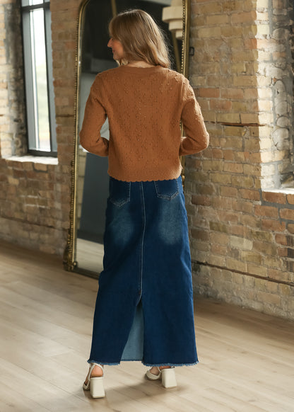 Waist-length camel knit cardigan from the back, styled with a dark wash denim maxi skirt.