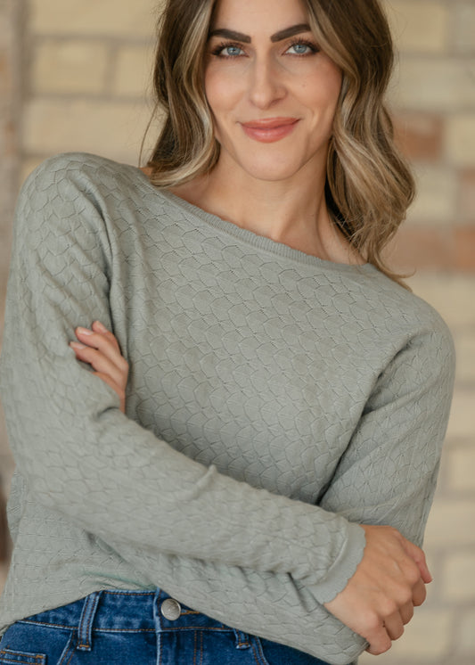 Sage pointelle sweater shown from the side, with long sleeves and scalloped cuffs above a denim skirt.