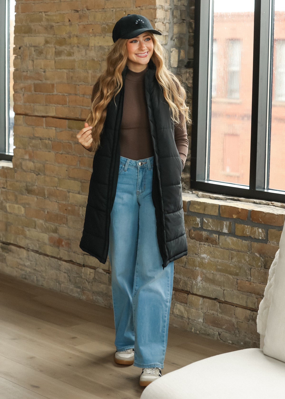 Full-length black puffer vest styled over a gray sweatshirt dress with sneakers.