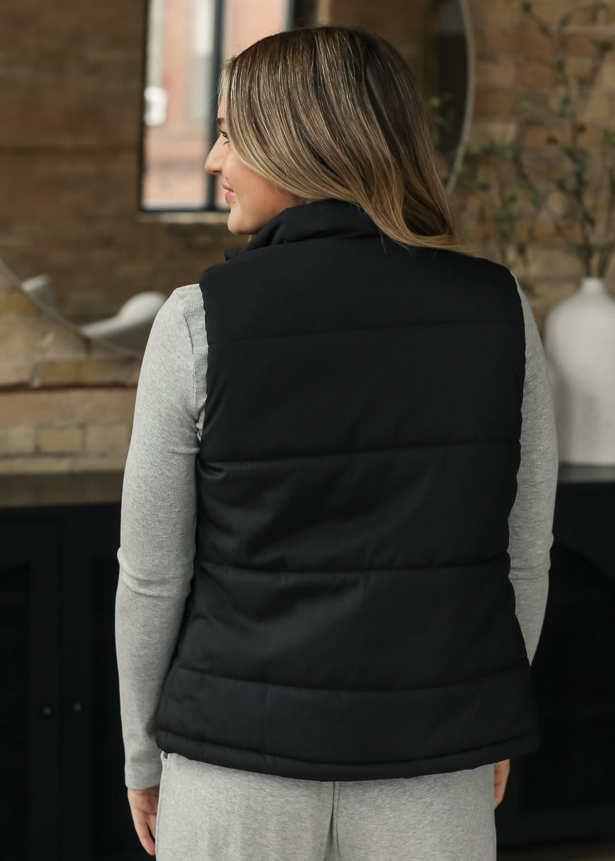 Back of black short puff vest showing the simple sleeveless silhouette.