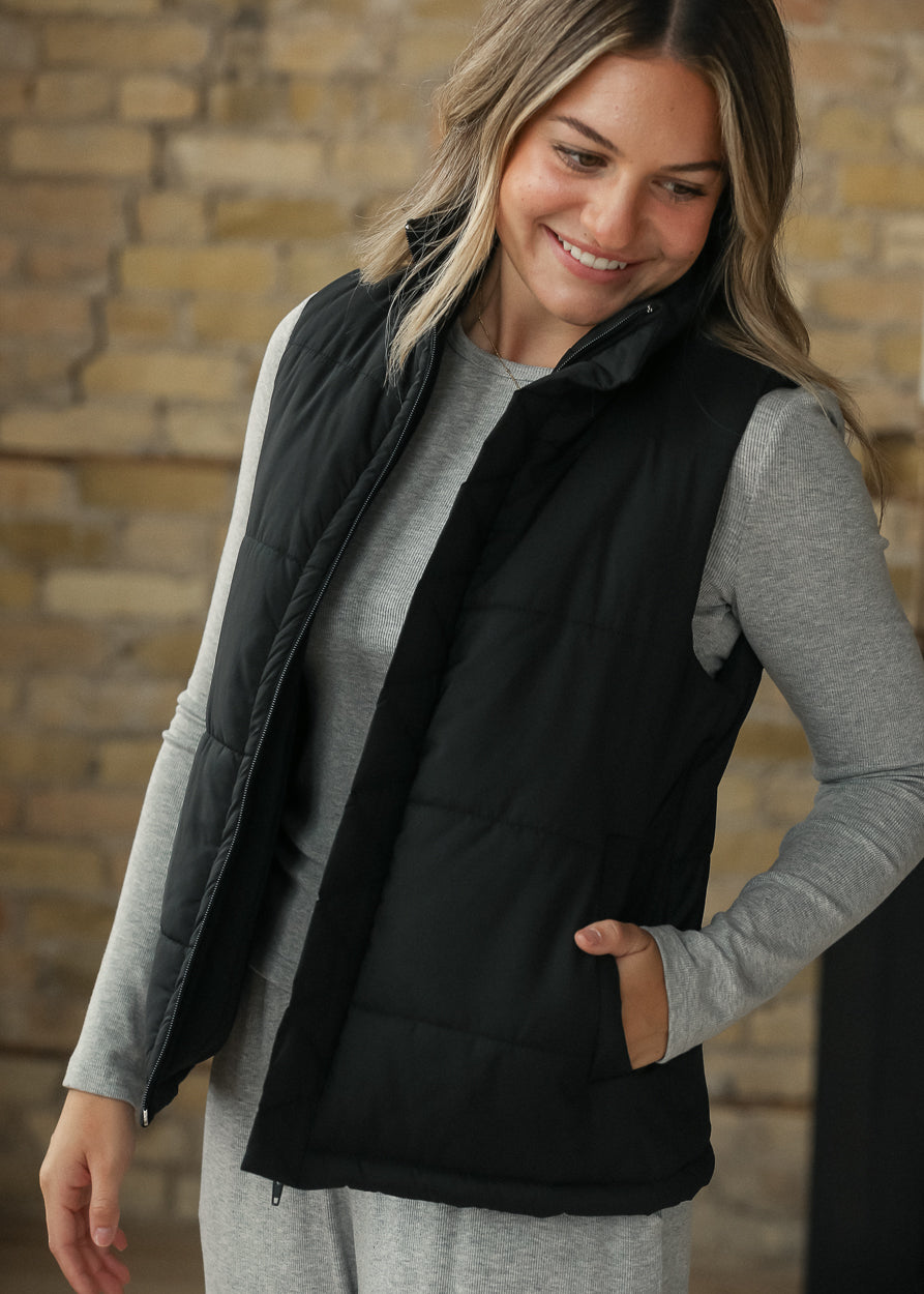 Black puff vest layered over an espresso top, showing the short sleeveless silhouette.