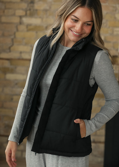 Black puff vest layered over an espresso top, showing the short sleeveless silhouette.