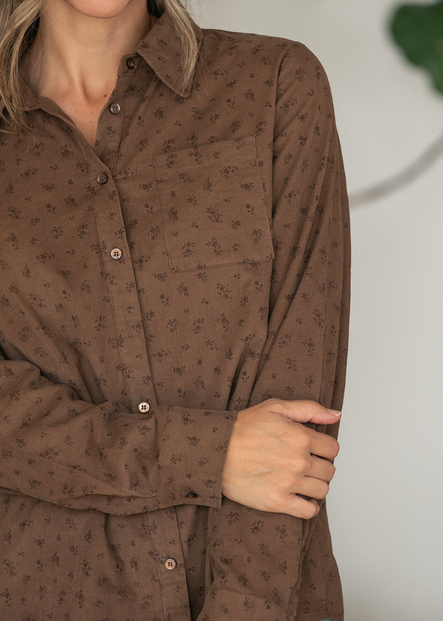 Close-up of brown corduroy shirt showing tiny floral print, front buttons, chest pocket, and long sleeve cuff.