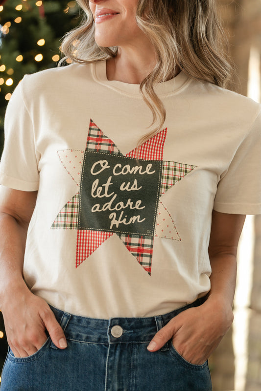 Close-up of ivory tee with “O Come Let Us Adore Him” lettering and a red and green quilt-style star graphic.