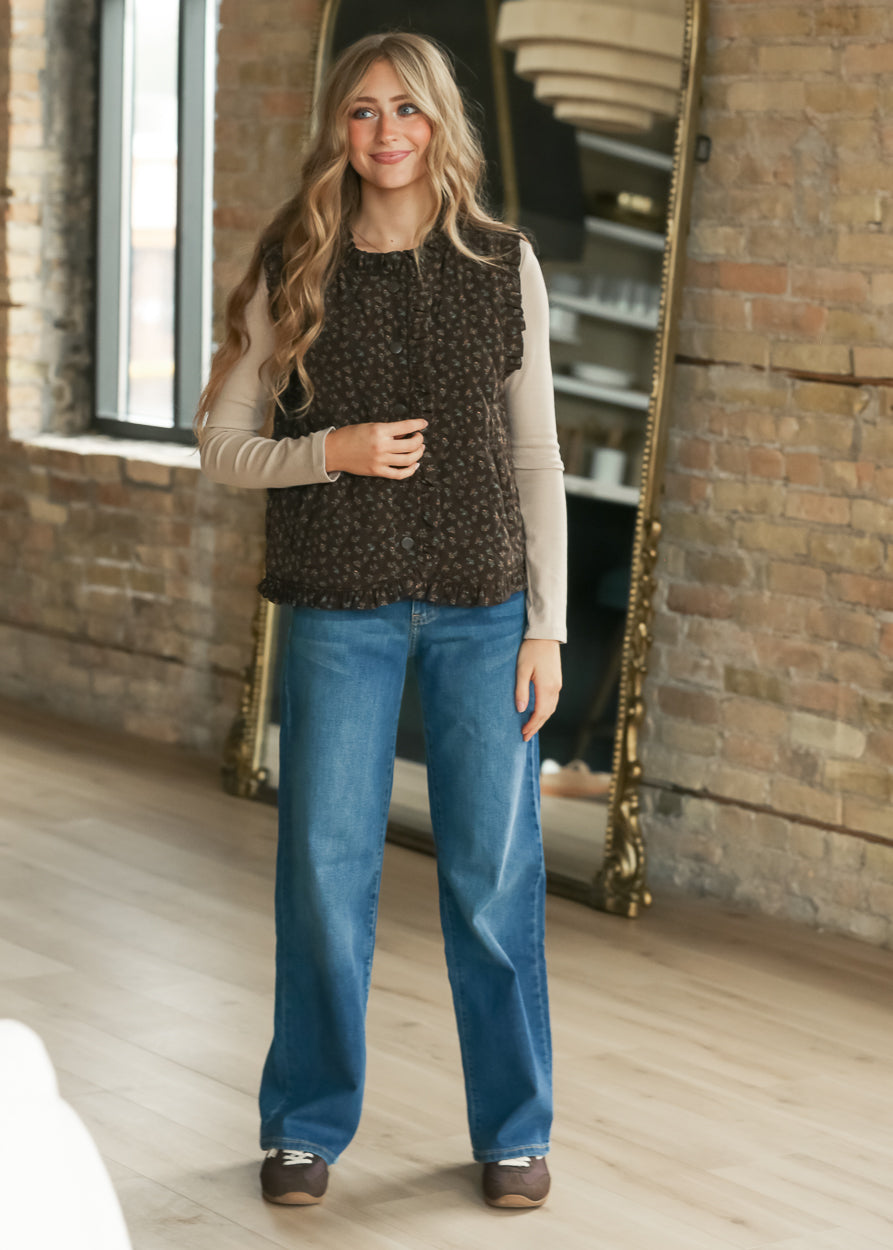 Dark brown floral quilted vest styled over a taupe long sleeve top with medium wash denim.