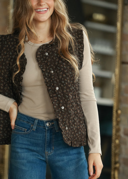 Dark brown floral quilted vest styled over a taupe long sleeve top with medium wash denim.
