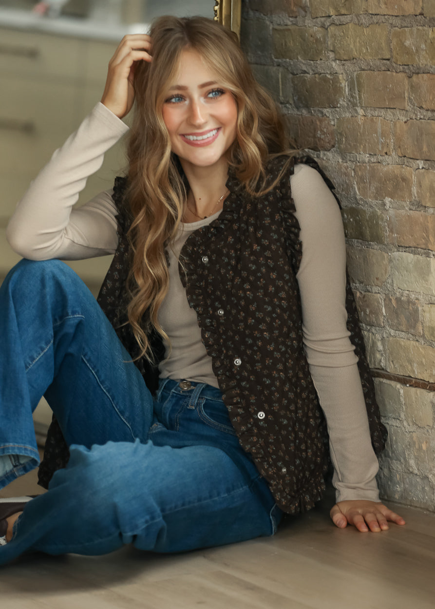 Dark brown floral quilted vest with ruffle trim and front snap detail, layered over a taupe ribbed top.