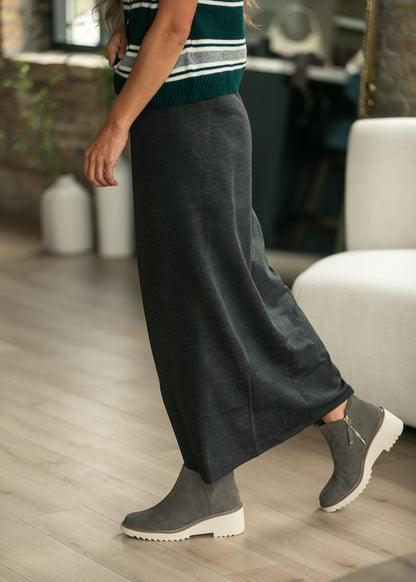 Close-up of charcoal gray knit maxi skirt hem grazing the ankle, styled with gray suede boots.