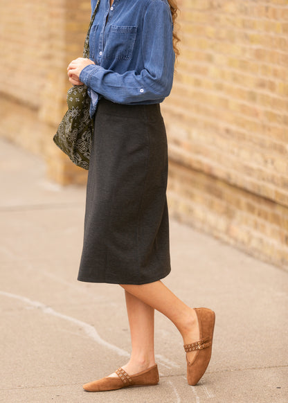 Close-up of charcoal gray knit midi skirt hem hitting mid-calf, styled with tan suede flats.