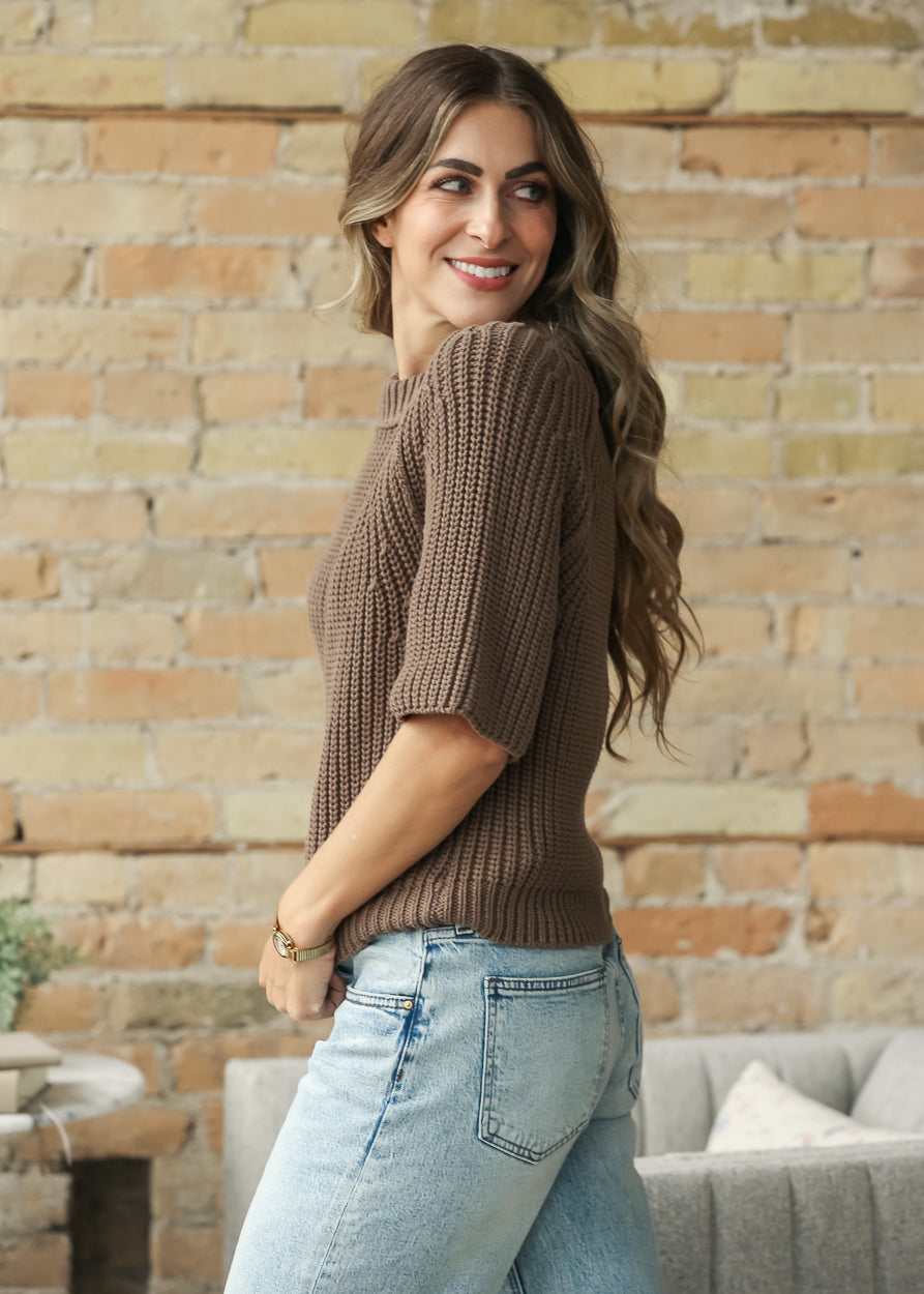 Brown raglan knit top with loose fit and elbow-length sleeves, styled with light wash denim.