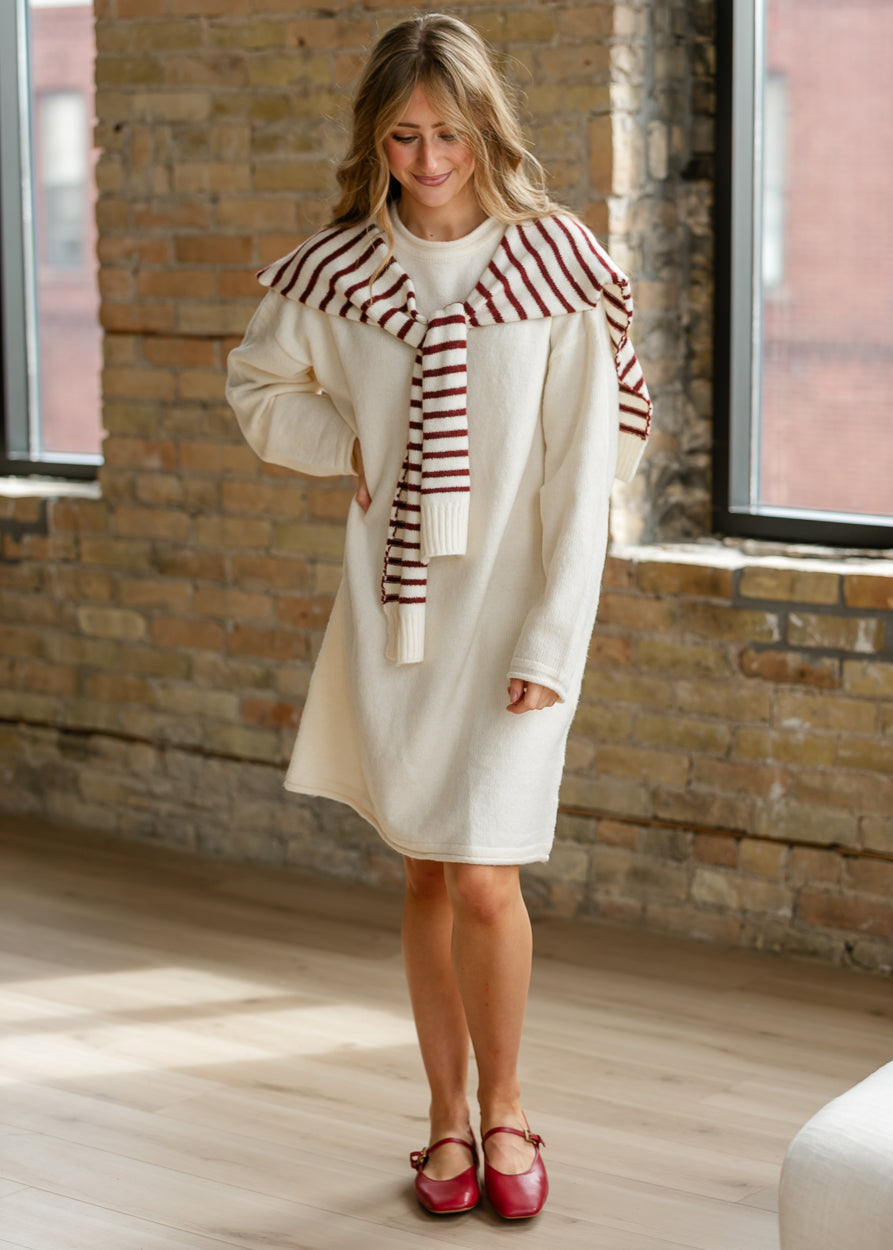 Knee-length cream sweater dress with loose fit, long sleeves, and red striped shawl.