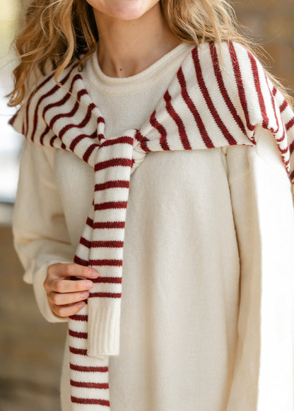 Close-up of cream sweater dress with red striped knit shawl tied at the shoulders.
