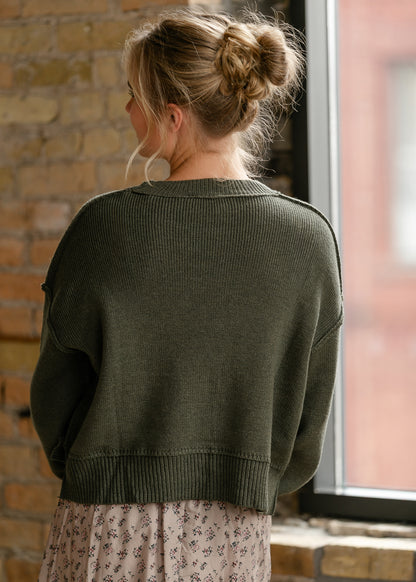 Back of olive green relaxed sweater showing drop shoulders, exposed seams, and a longer back hem.