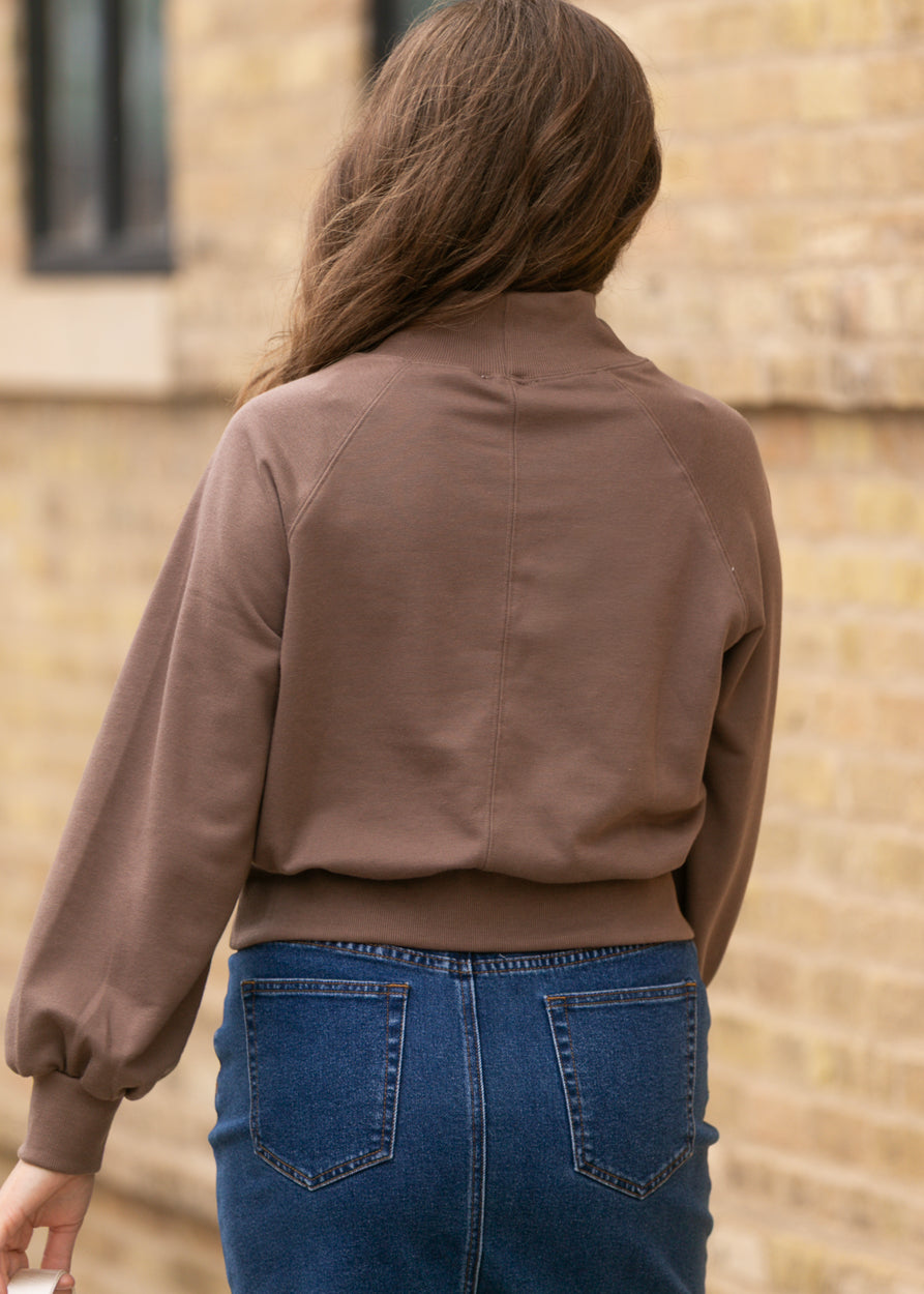Back of brown turtleneck sweater showing raglan seam detail, balloon sleeves, and ribbed hem.
