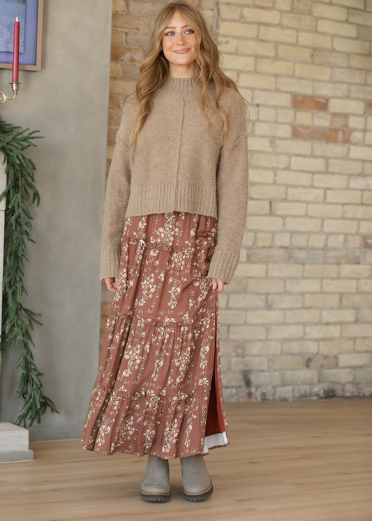 Brown floral midi skirt held slightly aside to show the slit and lining, styled with gray ankle boots.
