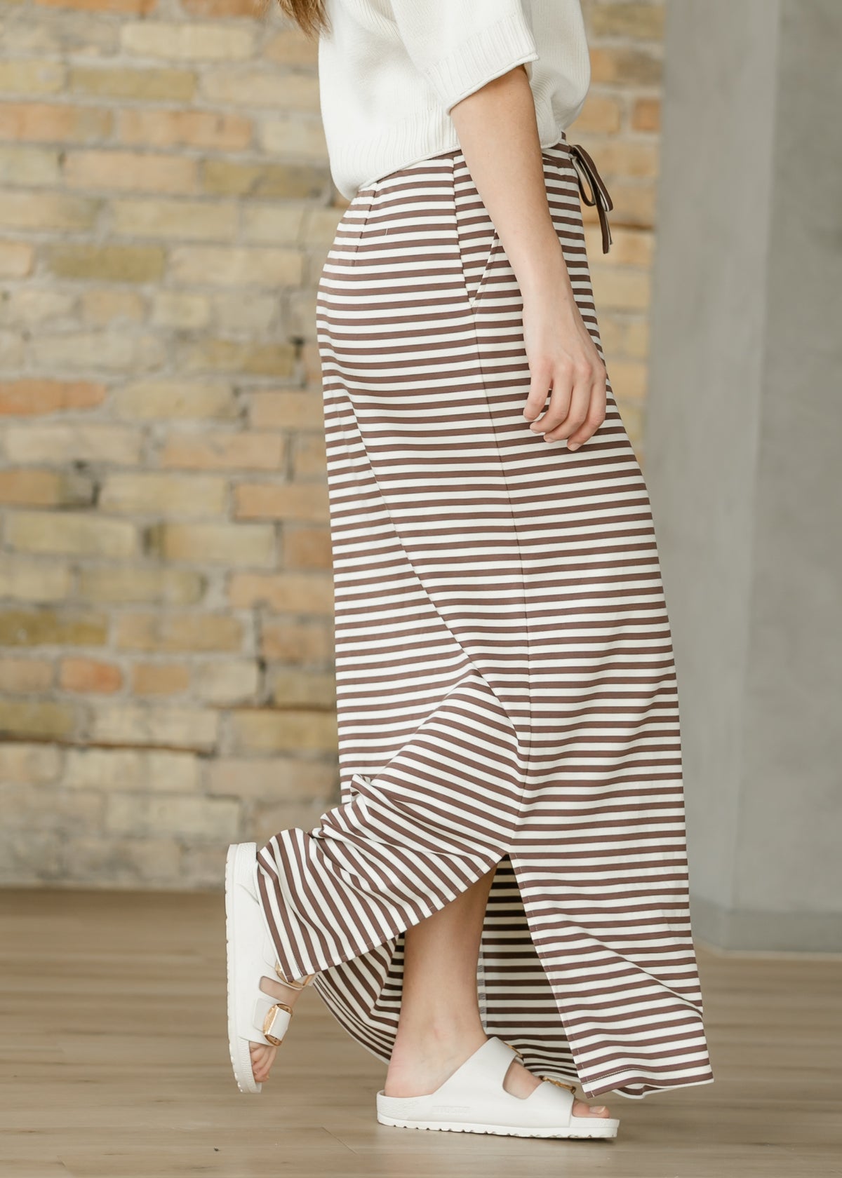Side view of chocolate stripe maxi skirt showing the pocket, long side slit, and full-length hem.