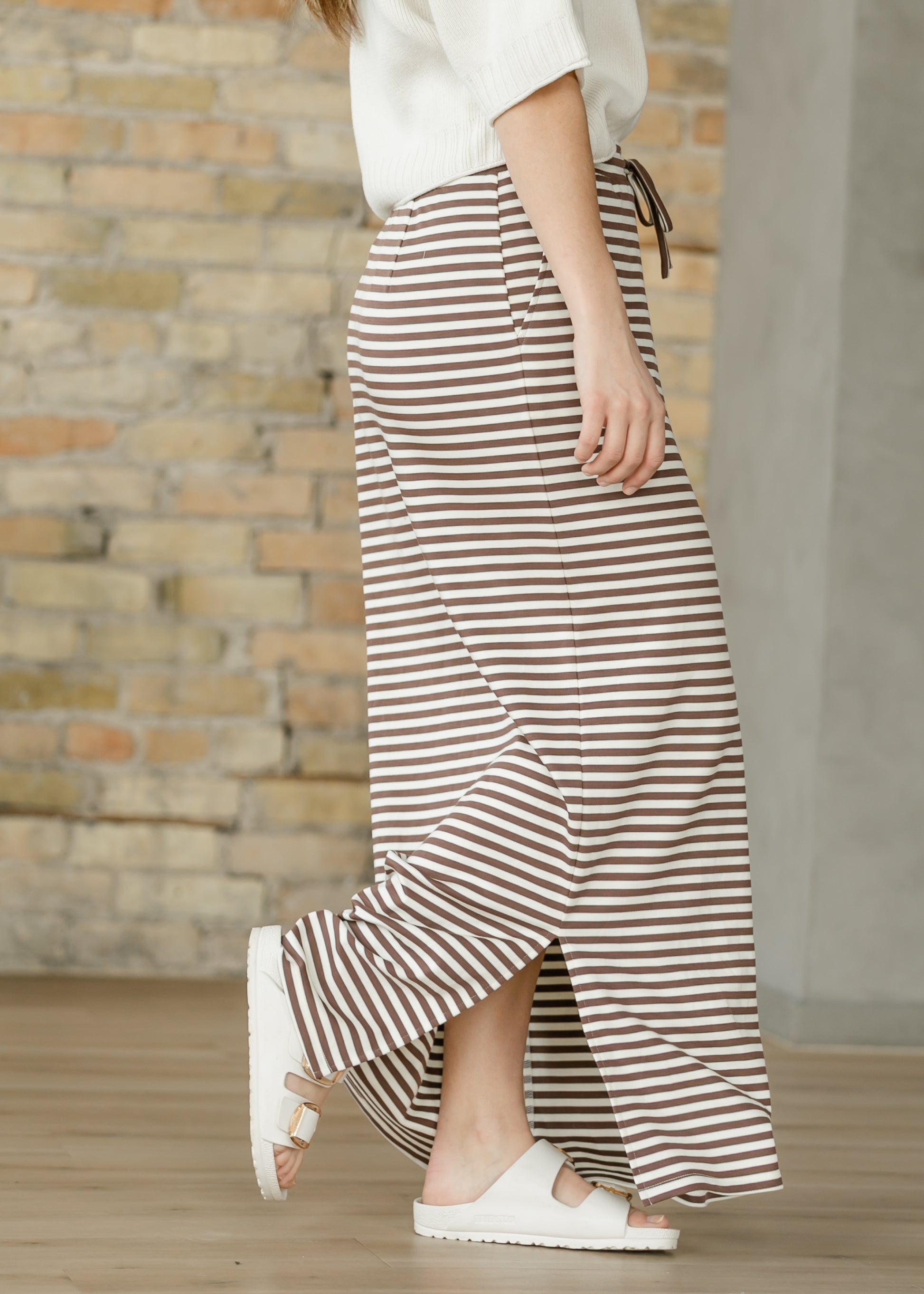 Side view of chocolate stripe maxi skirt showing the pocket, long side slit, and full-length hem.