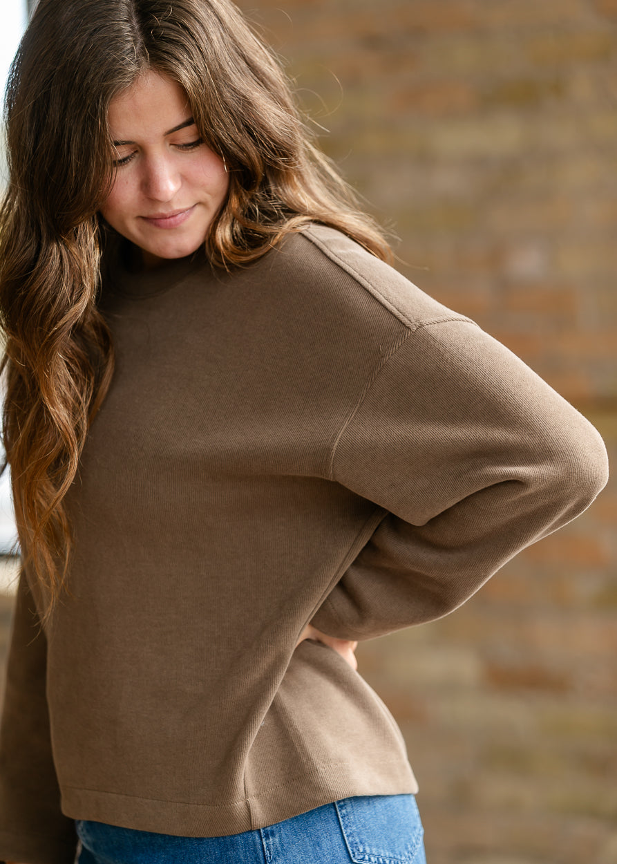 Loose-fit brown pullover sweater styled with a long denim skirt and neutral shoes.