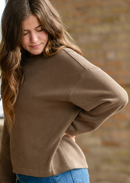 Loose-fit brown pullover sweater styled with a long denim skirt and neutral shoes.